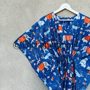 May include: A blue and orange kaftan with a winter animal print. The kaftan has a drawstring waist and is hanging on a white hanger.