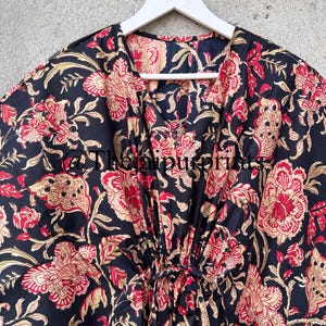 May include: Black cotton kaftan with a floral print in shades of red, gold, and cream. The kaftan has a V-neckline and a tie at the waist.