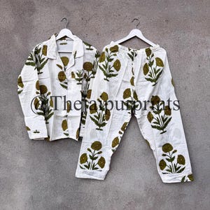 May include: White pajama set with a green floral pattern. The set includes a button-down shirt and matching pants, both hanging on white hangers. The text "The favour prints" is visible on the shirt.