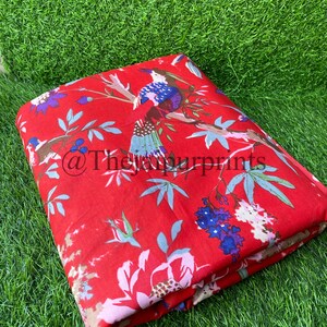Op de afbeelding: Rode stof met een bloemen- en vogelprint. De stof heeft een herhalend patroon van roze bloemen, groene bladeren en blauwe vogels.