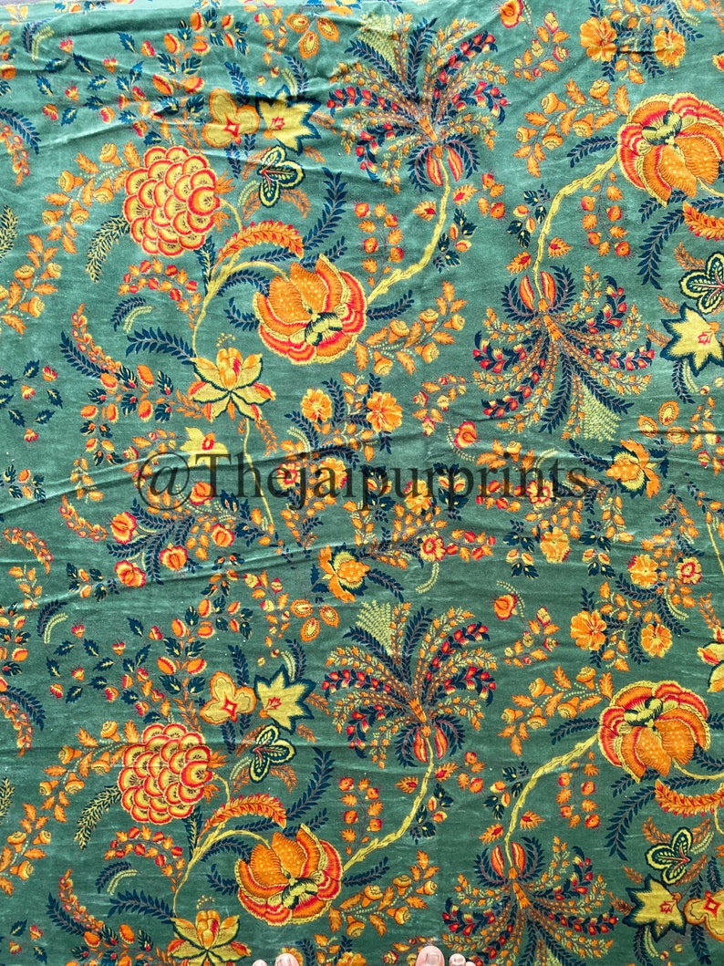 May include: A green fabric with a floral pattern. The flowers are orange, yellow, and red. The fabric has a vintage look.