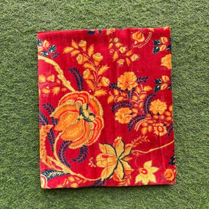 May include: Red fabric with a floral pattern in shades of orange, yellow, and black. The fabric has a vintage look and feel.