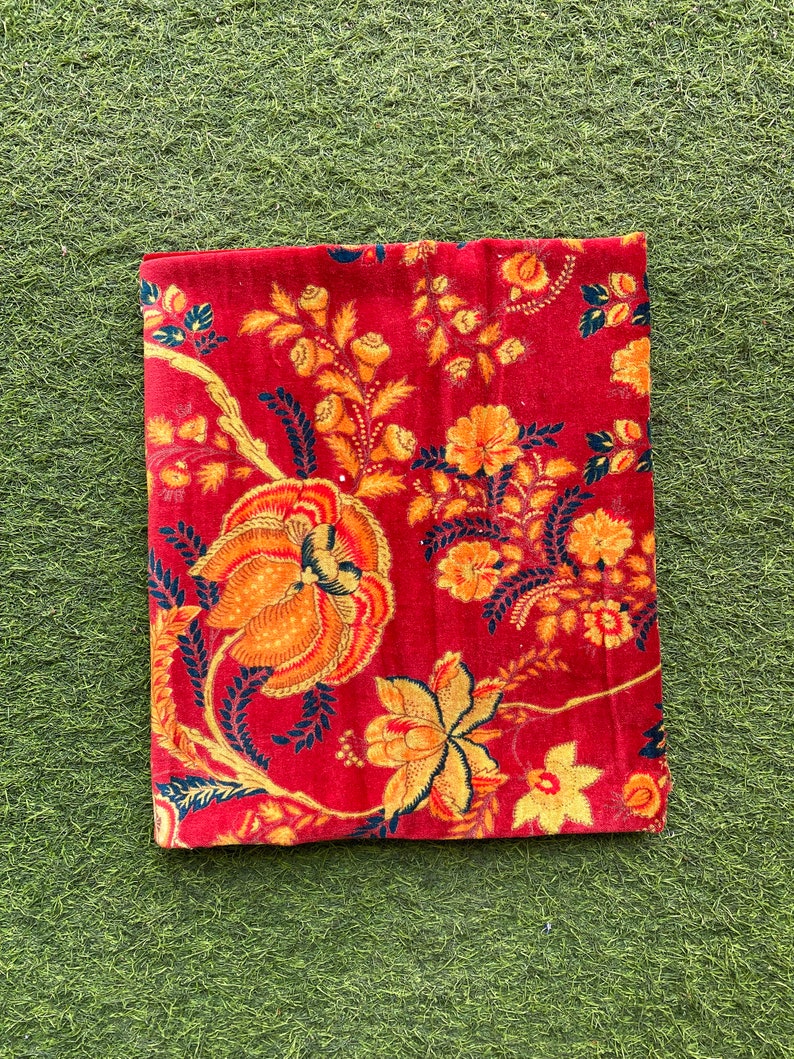 May include: Red fabric with a floral pattern in shades of orange, yellow, and black. The fabric has a vintage look and feel.