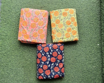 May include: Three fabric swatches with floral patterns. The first swatch is peach with orange flowers, the second is yellow with green leaves and orange flowers, and the third is navy blue with orange flowers.