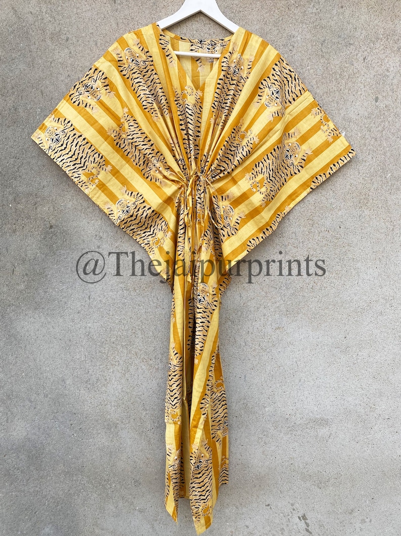 May include: Yellow and black striped kaftan dress with a tiger print design. The dress has a V-neck and a drawstring waist. The text "@Thejaipurprints" is visible in the lower left corner. The dress is hanging on a white hanger.
