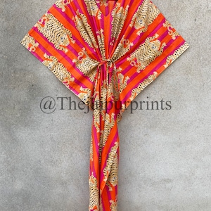 May include: An orange and pink patterned kaftan dress with a tiger print design. The dress has a V-neck and a tie at the waist. The fabric is lightweight and appears to be cotton. The Jaipur Prints is printed on the bottom left.