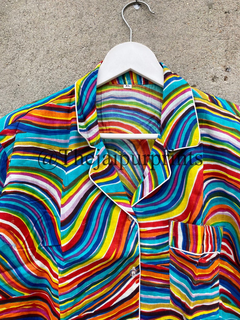 May include: A colorful striped shirt with a white collar and a pocket on the left side. The shirt has a wavy pattern and is made of a soft, silky fabric. The shirt is hanging on a white hanger.