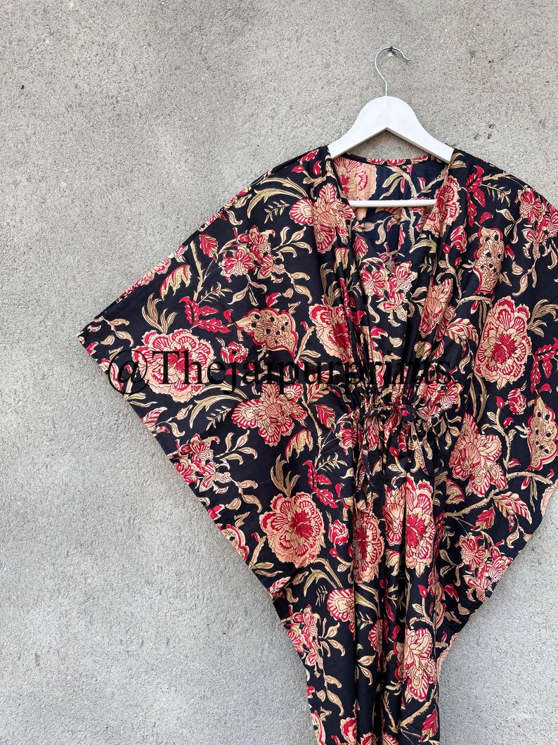 May include: Black floral print kaftan with a V-neck and a tie at the waist.