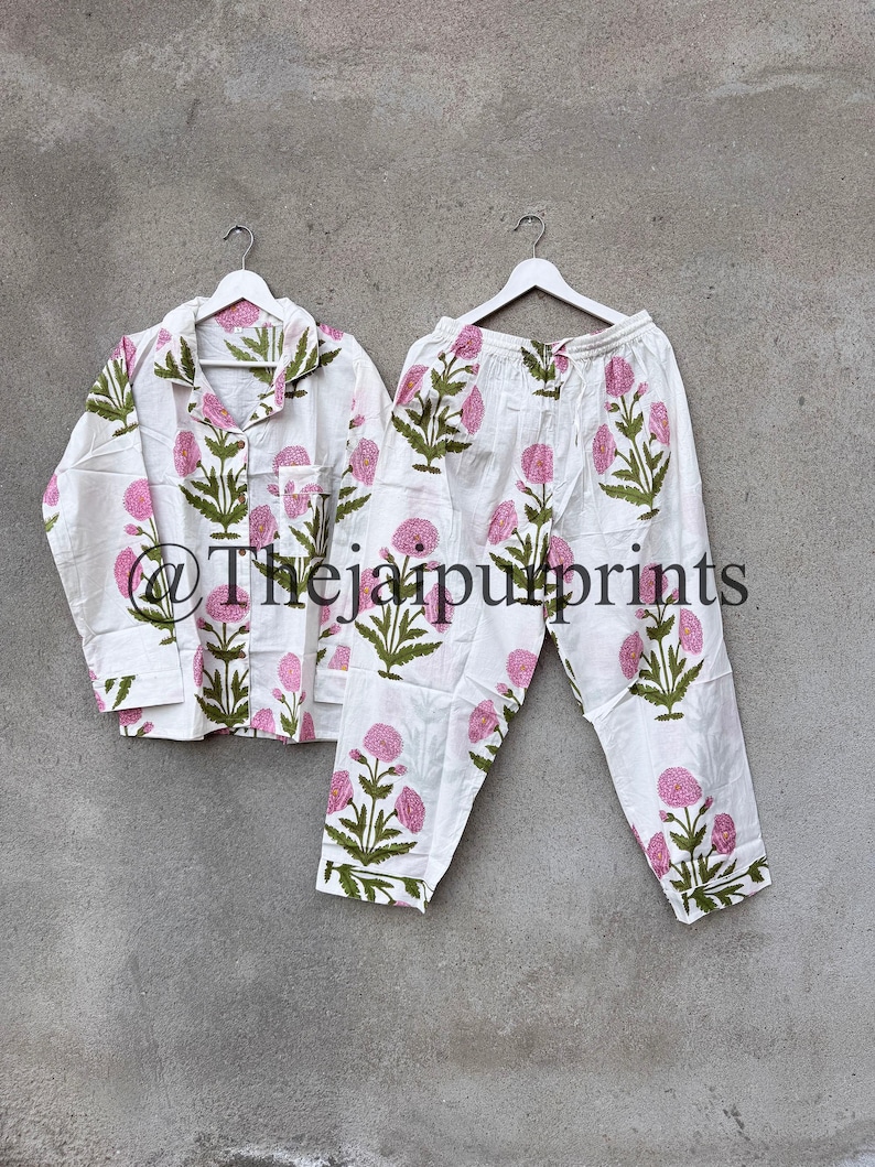 May include: White pajama set with a pink floral pattern and green leaves. The set includes a button-down shirt with a chest pocket and matching pants. The text "@Thejaipurprints" is visible on the bottom of the image.