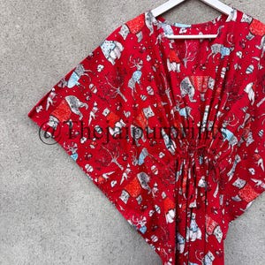 May include: Red cotton kaftan with a colorful print of animals and houses. The kaftan has a V-neck and a tie at the waist.