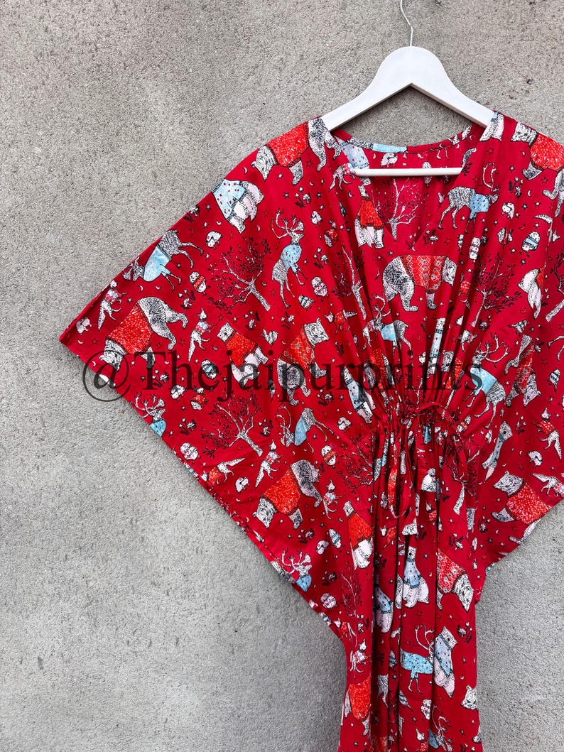 May include: Red cotton kaftan with a colorful print of animals and houses. The kaftan has a V-neck and a tie at the waist.