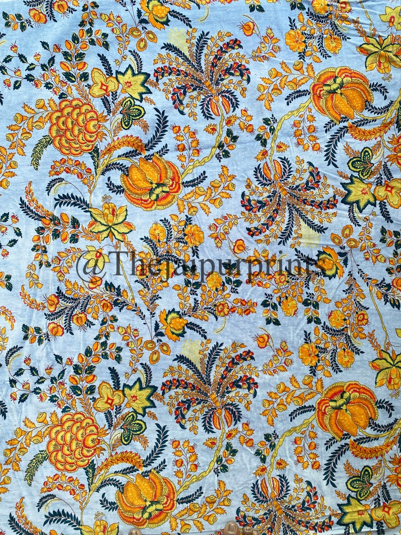 May include: A blue fabric with a floral pattern in shades of yellow, orange, and green. The flowers are stylized and have a vintage feel.