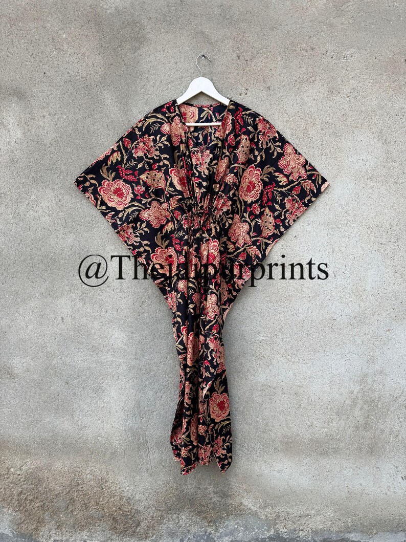 May include: A black and floral print kaftan with a V-neckline and a tie at the waist. The kaftan has a long, flowing silhouette and is perfect for a relaxed, bohemian look. @TheHappyPrints