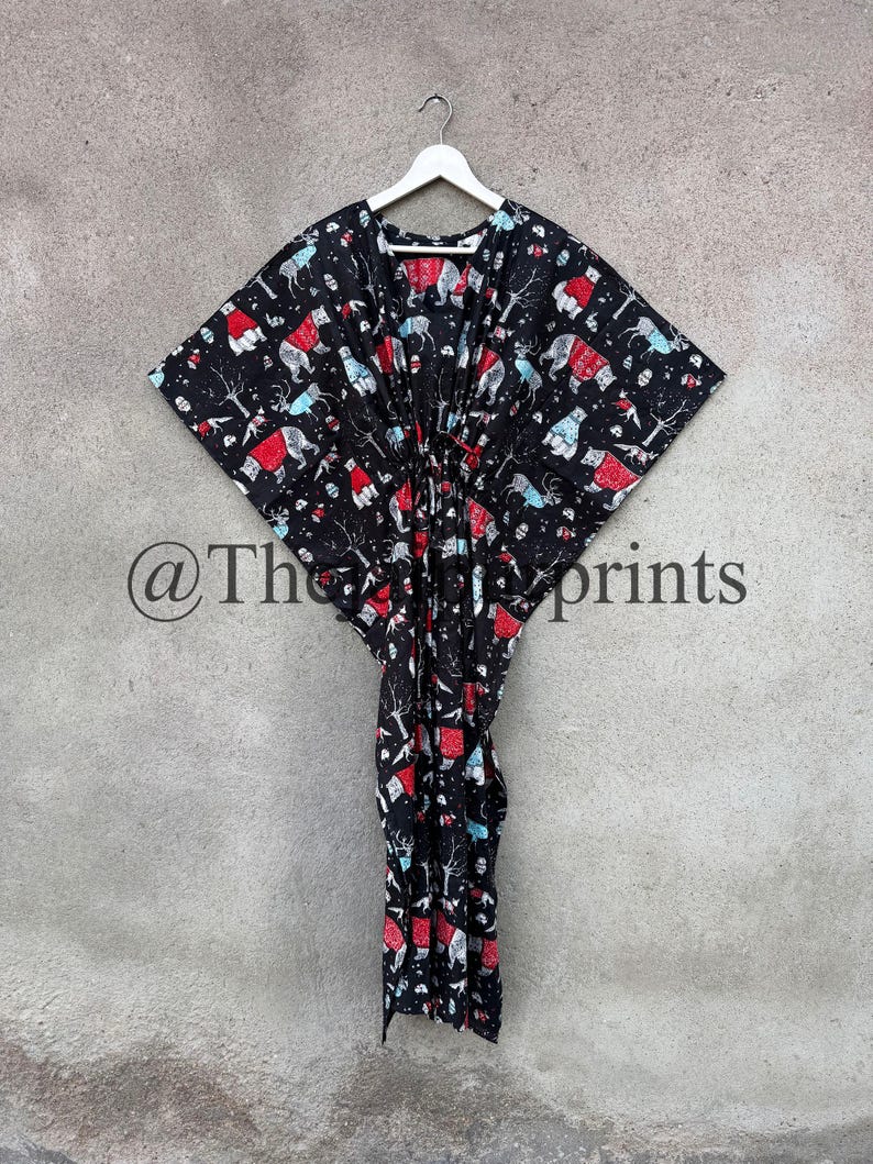 May include: A black kaftan with a white hanger. The kaftan has a red and blue print of polar bears wearing red hats and scarves. The print also includes trees and other wintery elements. The kaftan has a drawstring at the waist.