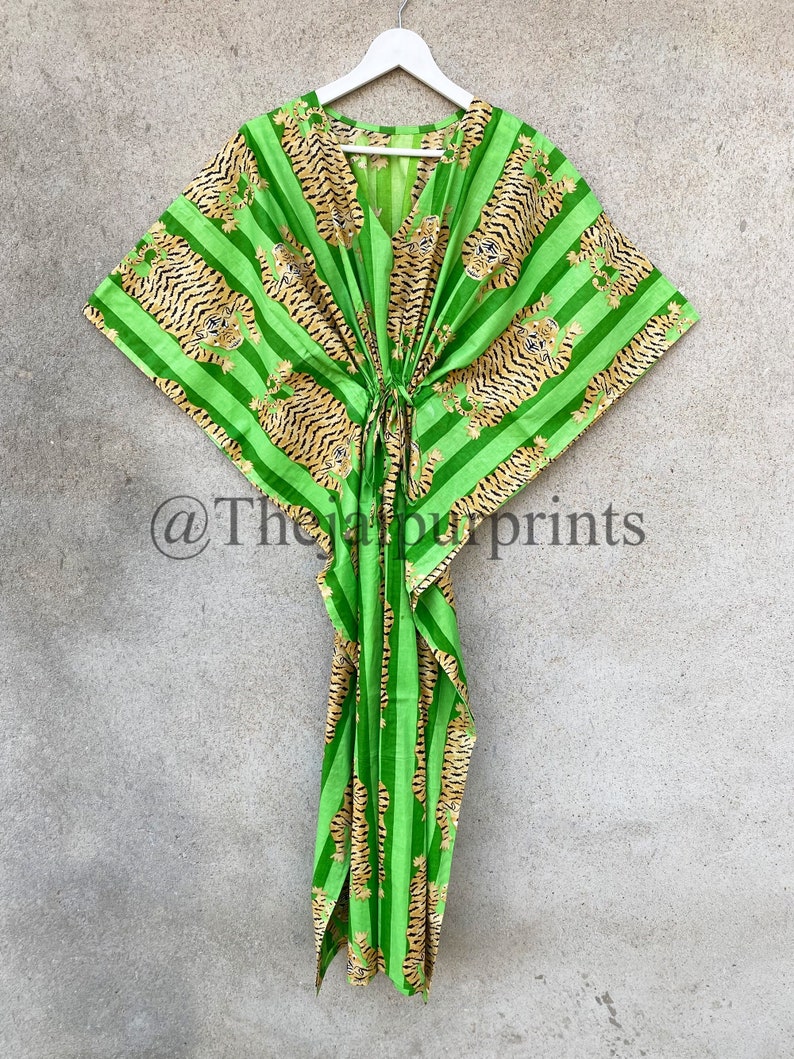 May include: A green kaftan with a V-neck and a tie closure. The fabric features a striped pattern with tiger illustrations in shades of brown and black. The garment is hanging on a white hanger against a neutral background.