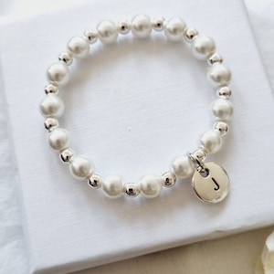 May include: A white pearl bracelet with a silver charm featuring the letter "J".
