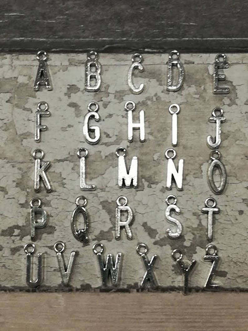 May include: A set of 26 silver metal alphabet letter charms. Each letter is separate and has a small loop at the top for attaching to a chain or bracelet.