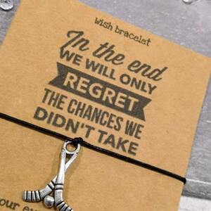 May include: A black string bracelet with a silver hockey stick charm. The bracelet card reads "In the end we will only regret the chances we didn't take".