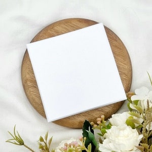May include: A blank white card on a wooden coaster with white flowers in the background.