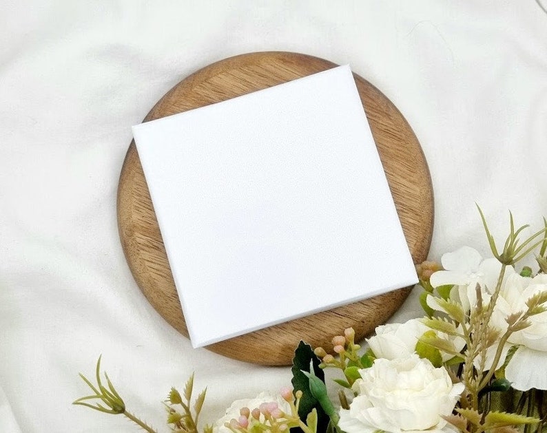 May include: A blank white card on a wooden coaster with white flowers in the background.