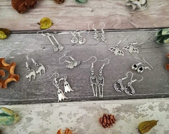 Może przedstawiać: Kolekcja 12 par srebrnych kolczyków w stylu Halloween. Kolczyki mają różne wzory, w tym nietoperze, duchy, szkielety, koty, miotły i zęby.
