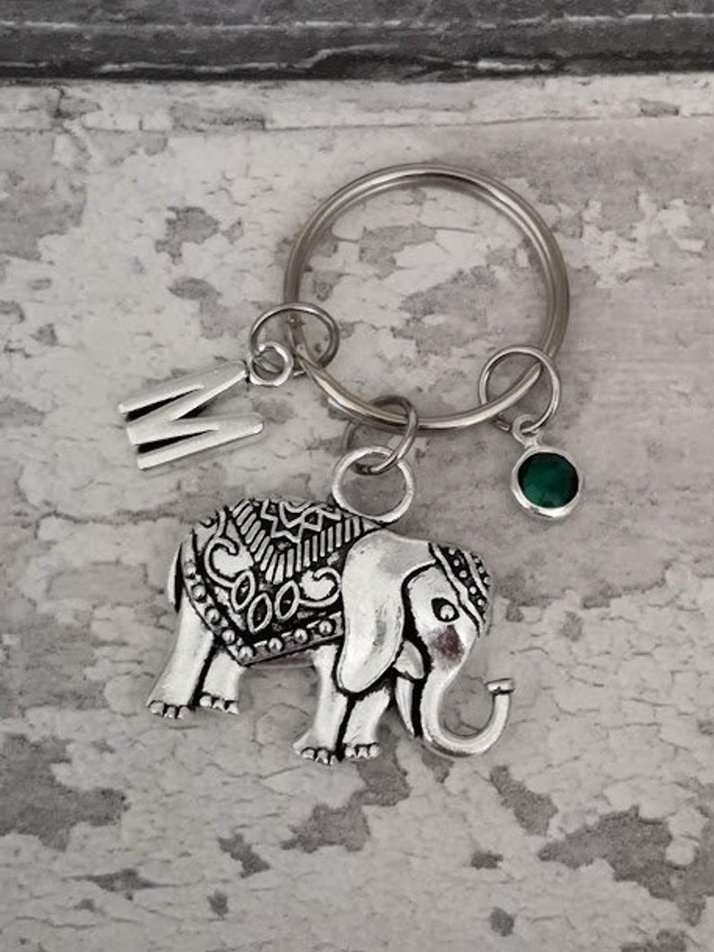 Pu&ograve; includere: Portachiavi in ​​argento con un ciondolo a forma di elefante dettagliato, un ciondolo con una gemma verde e un ciondolo in argento con la lettera M.