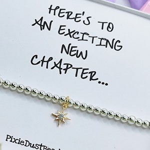 May include: A silver beaded bracelet with a gold star charm featuring a clear crystal. The bracelet is packaged in a white box with the text "Here's to an exciting new chapter..." and the website address "PixieDustBeads.etsy.com".