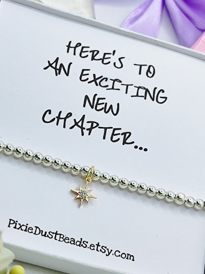 May include: A silver beaded bracelet with a gold star charm featuring a clear crystal. The bracelet is packaged in a white box with the text "Here's to an exciting new chapter..." and the website address "PixieDustBeads.etsy.com".