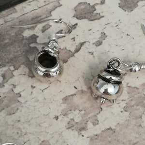 May include: A pair of silver cauldron earrings. The earrings are made of metal and have a detailed design.