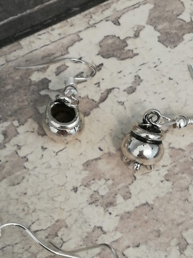 May include: A pair of silver cauldron earrings. The earrings are made of metal and have a detailed design.