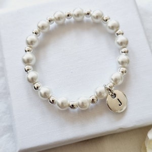 May include: A white pearl bracelet with a silver charm featuring the letter "J".