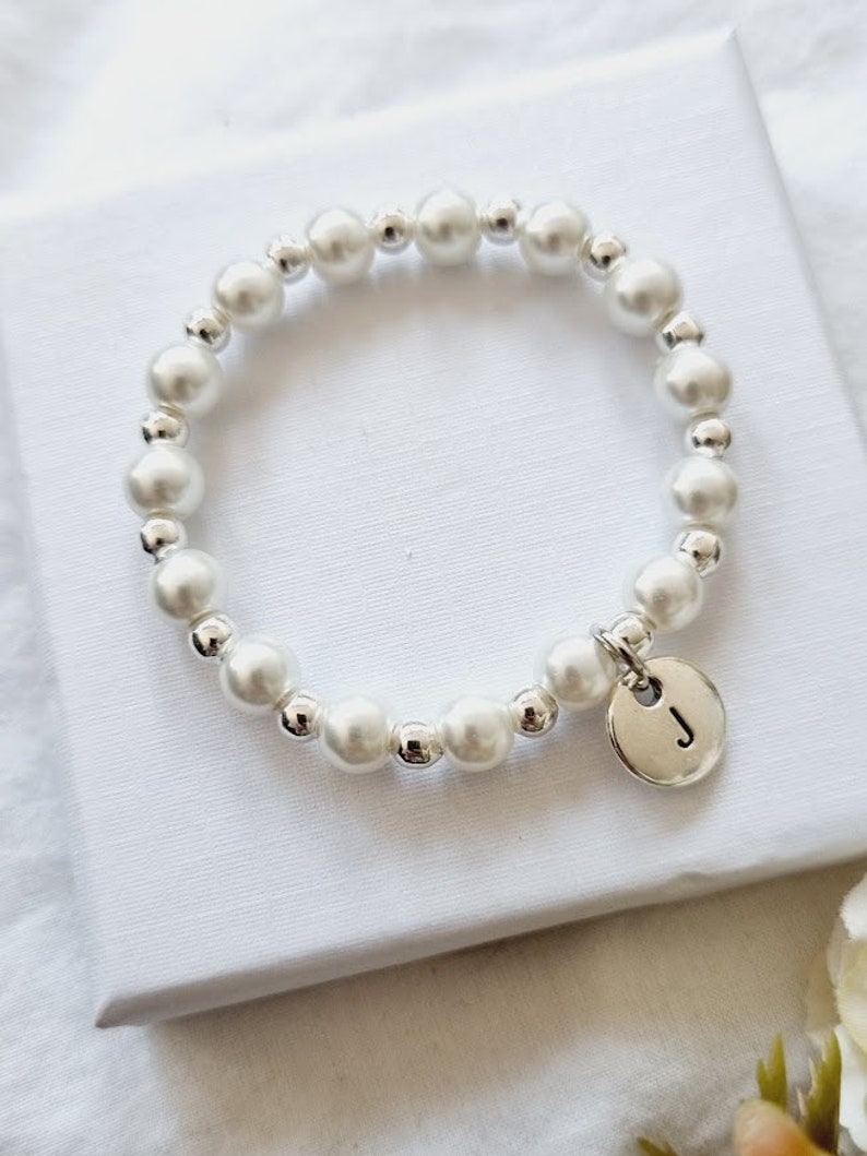 May include: A white pearl bracelet with a silver charm featuring the letter "J".