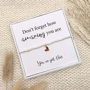 May include: A silver beaded bracelet with a gold heart charm, displayed on a white card in a white box. The card features the text "Don't forget how amazing you are" and "You've got this" in black script.