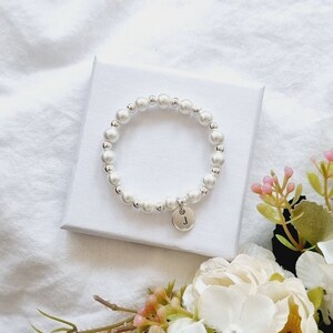May include: A white pearl bracelet with a silver charm featuring the letter "J".