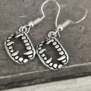 May include: A pair of silver earrings with a detailed design of teeth. The earrings are hanging from silver hooks.
