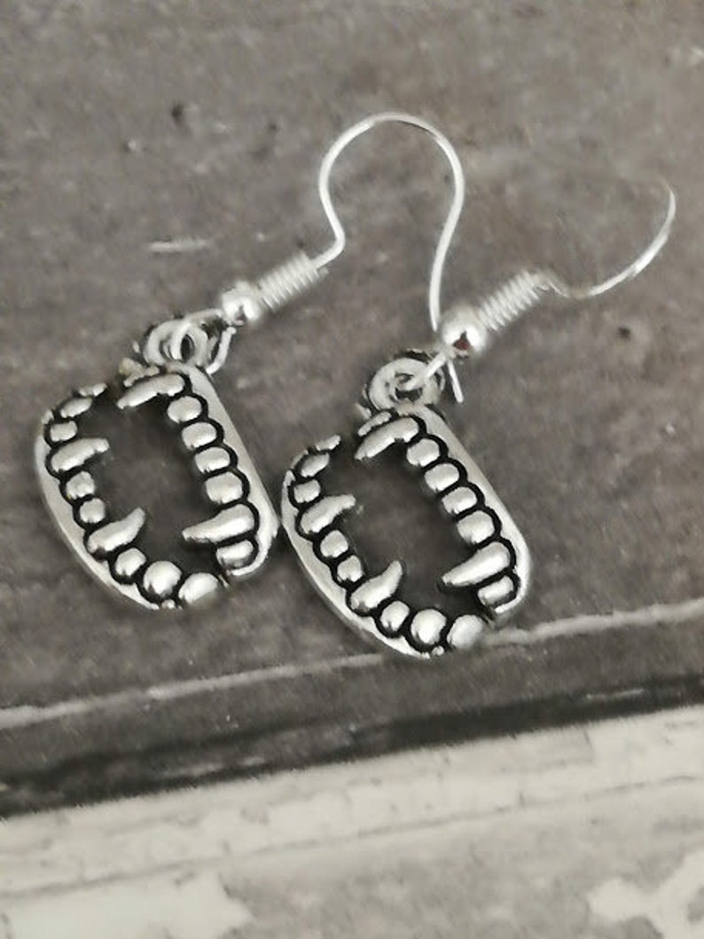 May include: A pair of silver earrings with a detailed design of teeth. The earrings are hanging from silver hooks.