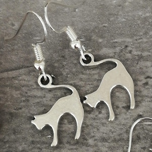 May include: A pair of silver cat silhouette earrings. The earrings are dangle style and feature a simple cat design.