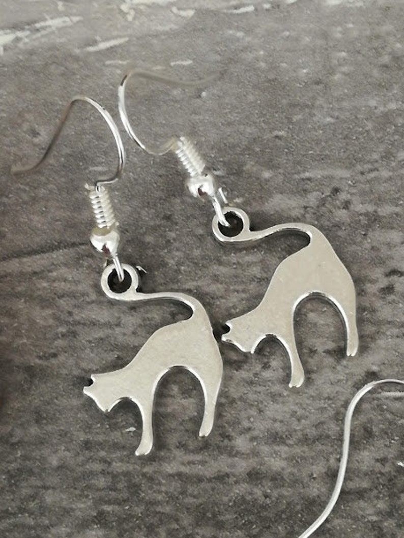 May include: A pair of silver cat silhouette earrings. The earrings are dangle style and feature a simple cat design.
