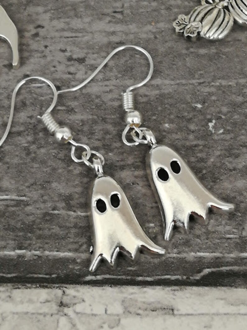May include: A pair of silver ghost earrings. Each ghost has two black eyes.