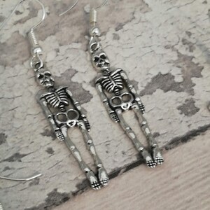 May include: A pair of silver skeleton dangle earrings. The earrings are made of metal and feature a detailed skeleton design.