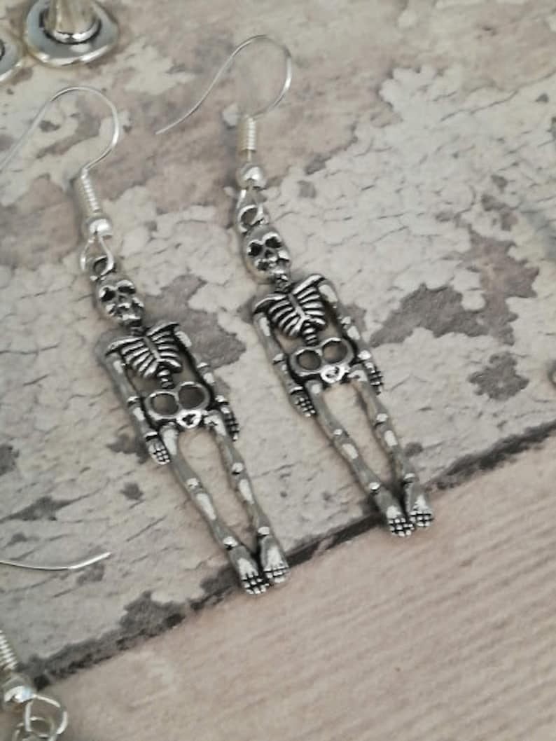 May include: A pair of silver skeleton dangle earrings. The earrings are made of metal and feature a detailed skeleton design.