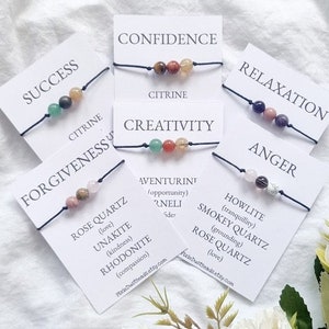 May include: Six bracelets with different coloured stones and black string. Each bracelet has a card with a word on it, such as "Success", "Confidence", "Creativity", "Relaxation", "Anger", and "Forgiveness". The cards also list the types of stones used in each bracelet.