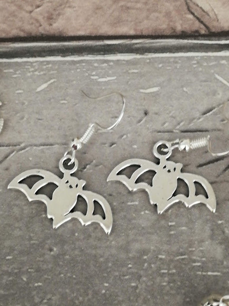 May include: A pair of silver earrings with a bat design. The bats are detailed with wings and a body.