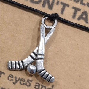 May include: A black cord bracelet with a silver charm of two crossed hockey sticks and a puck. The bracelet has the text "Take Chances You Didn't Take" on the card.