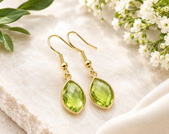 May include: A pair of gold-toned drop earrings featuring faceted, marquise-cut lime green stones set in metal bezels. The earrings are attached to gold-toned fishhook wires, showcasing a clear, geometric design with a polished finish.