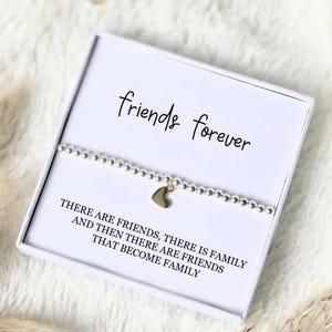 Może przedstawiać: Srebrna bransoletka z koralików ze złotym sercem, zapakowana w białe pudełko. Pudełko zawiera napis "friends forever" i cytat o przyjaźni. Przemyślany prezent dla przyjaciela.