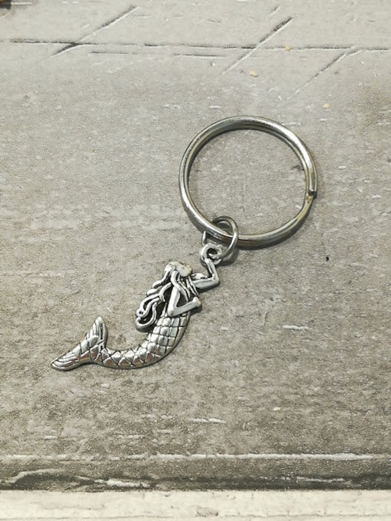 May include: Silver mermaid keychain with a silver key ring. The mermaid is depicted with long flowing hair and a tail.