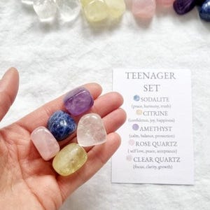 May include: A collection of five tumbled gemstones including purple amethyst, blue sodalite, pink rose quartz, yellow citrine, and clear quartz. A white information card labelled TEENAGER SET lists the stones and their properties.