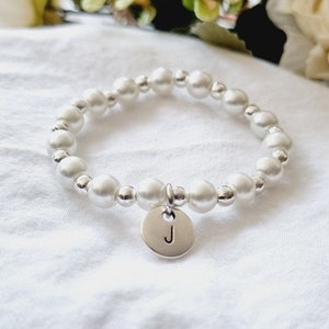 May include: A white pearl bracelet with a silver charm that has the letter "J" on it.