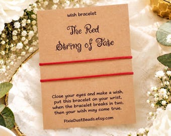 May include: A rectangular kraft paper card featuring the text "wish bracelet" and "The Red String of Fate" with two thin red strings stretched horizontally across the center. Below the strings, the card includes printed instructions.